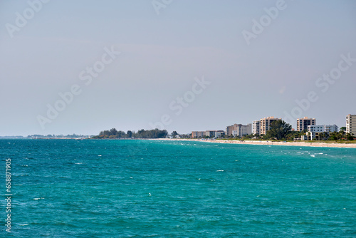 Resort beach with white sand, blue water, tall hotel buildings. Happy people sunbathing and swimming in ocean