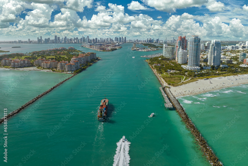 View from above of big container ship entering main channel in Miami harbor near South Beach high luxurious hotels and apartment buildings View from above of big container ship entering main channel in Miami harbor near South Beach high luxurious hotels and apartment buildings