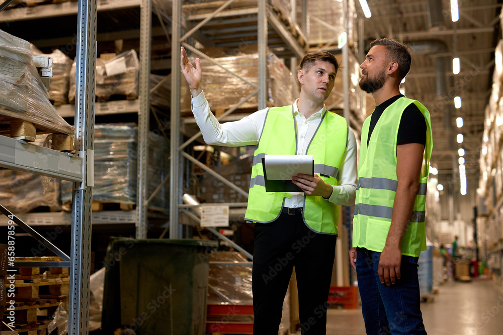 Caucasian two engineers in uniform, checking goods and supplies on shelves in warehouse. logistic and business export. Concept of good management system to support working with industrial business.