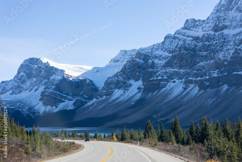 Beautiful scenery of a long curved road surrounded by high snowy rocky mountains, under blue sky