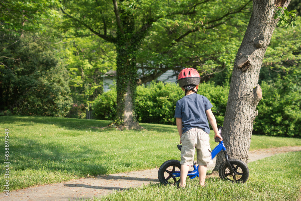 Young boy preparing to ride balance bike on suburban sidewalk. Young boy preparing to ride balance bike on suburban sidewalk.