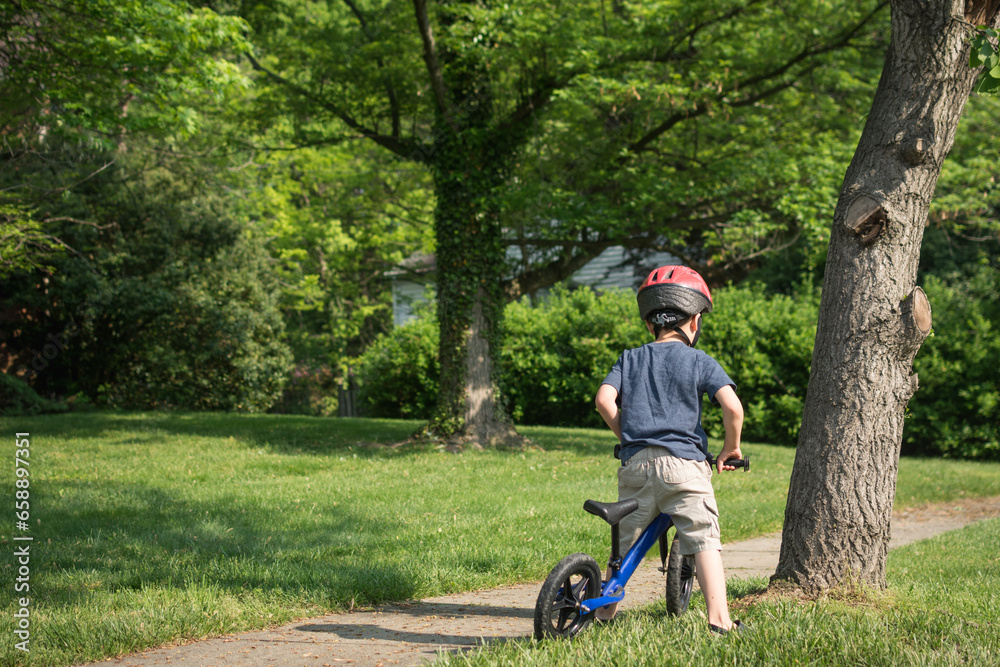 Young boy preparing to ride balance bike on suburban sidewalk. Young boy preparing to ride balance bike on suburban sidewalk.