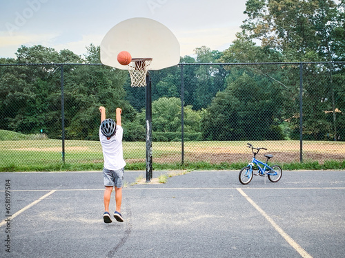 Φωτογραφία Young boy playing basketball on blacktop of suburban playground.