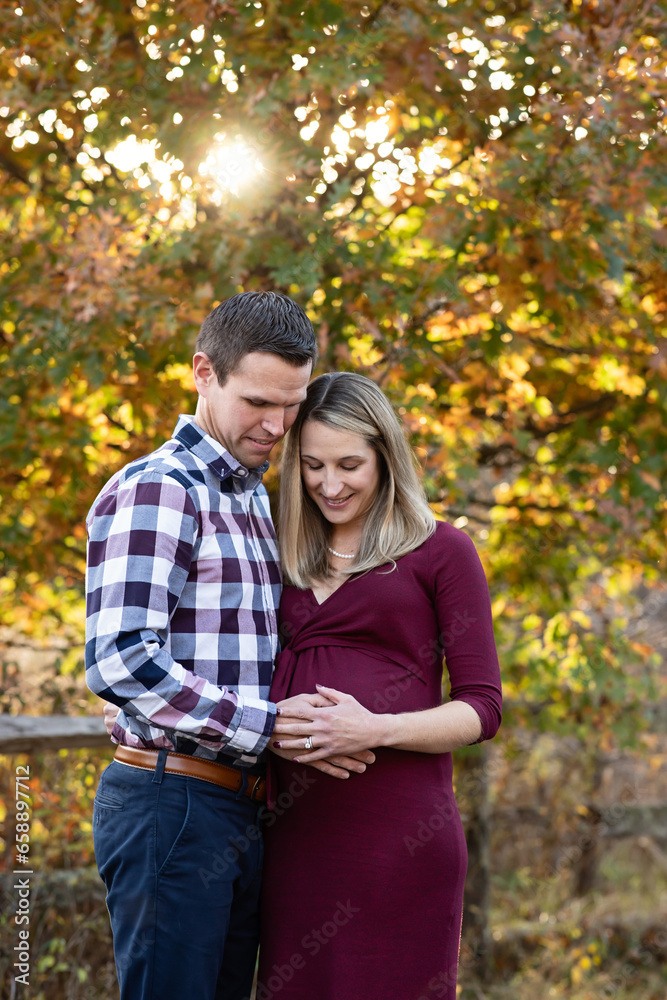 Expecting couple embracing, hands on mother's belly, fall backdrop