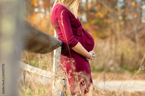 Close up of woman leaning against a fence holding pregnant belly photo