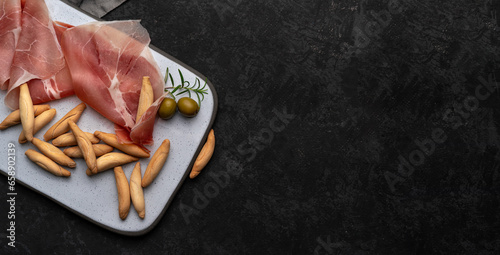 Flat lay with Spanish jamon and picos - bread sticks on dark table and grey desk, copy space. Snack from Spain concept