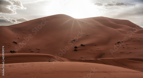 Desert dunes landscape with sun flare on cloudy sky background.