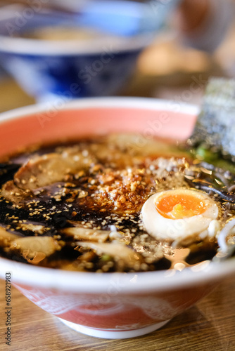 A bowl of tonkotsu ramen with black garlic sauce, chargrilled chashu pieces, bamboo shoots, soft-boiled egg and ladle spoons at Mikazuki, a Japanese restaurant in Sydney