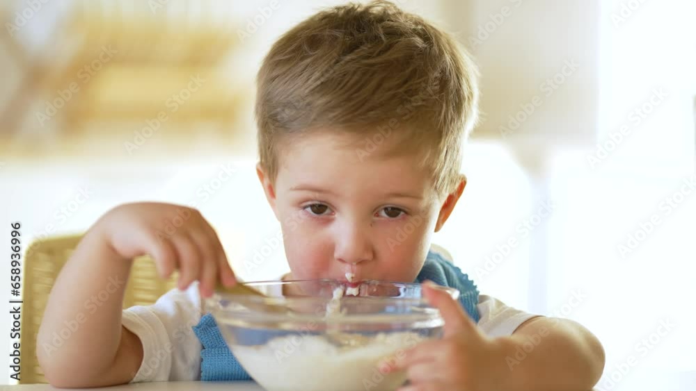 baby eats cereal porridge.Child sits at table and eats porridge.Family breakfast in kitchen.Child at table in kindergarten.Child proper nutrition.Breakfast in kindergarten.Happy dirty child with spoon baby eats cereal porridge.Child sits at table and eats porridge.Family breakfast in kitchen.Child at table in kindergarten.Child proper nutrition.Breakfast in kindergarten.Happy dirty child with spoon