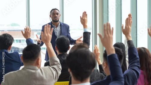 african american business man standing and talking in font of group of diversity business people in meeting at seminar listener raising hand to ask question. black speaker giving lecture photo