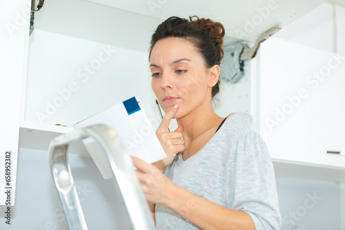 female reading manual to assemble cabinet in the kitchen