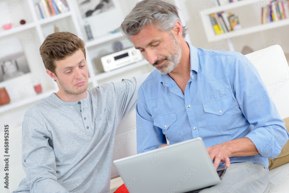 Man using laptop, younger man making facial expression of incomprehension Man using laptop, younger man making facial expression of incomprehension