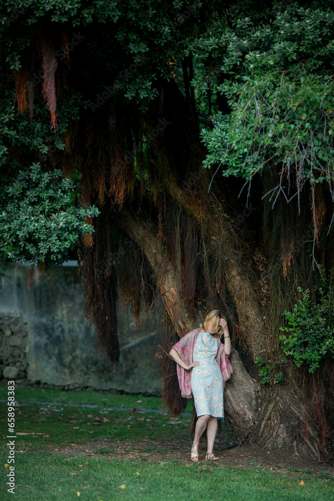 A woman is waiting for a date by a big tree in the park. A woman is waiting for a date by a big tree in the park.