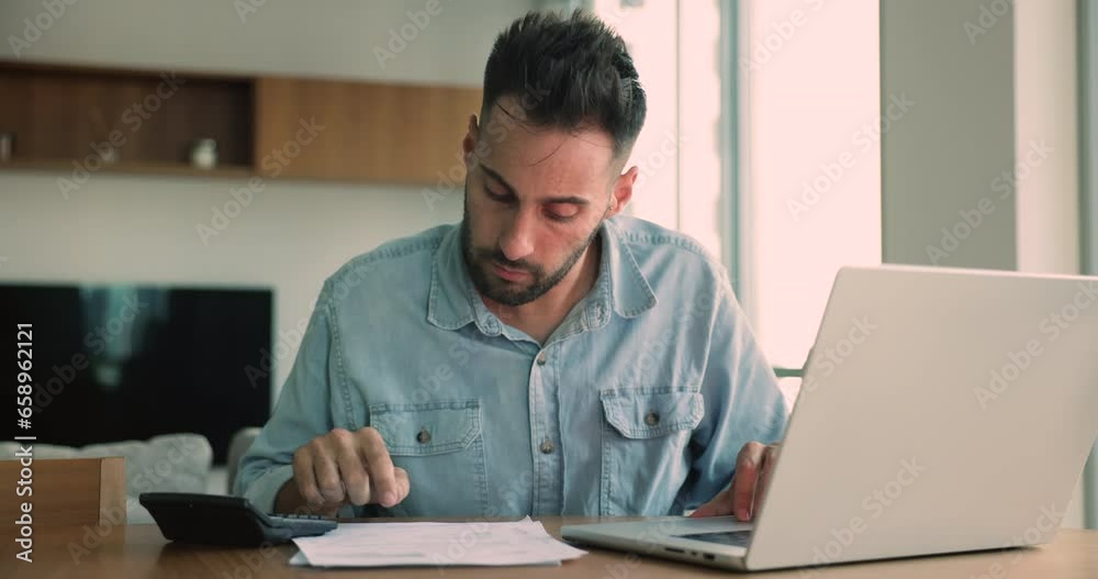 Depressed young Hispanic man sit at desk doing paperwork, pay bills, unpaid taxes online, feels worried about financial problems thinking of bank loan debt, money loss, bankruptcy or business issues