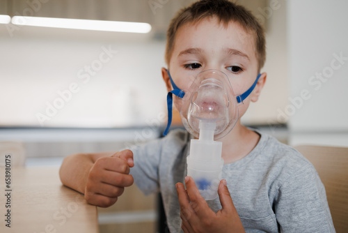 Sick little boy making inhalation with nebulizer to reduce coughing at home, child taking medication while breathing in through face mask