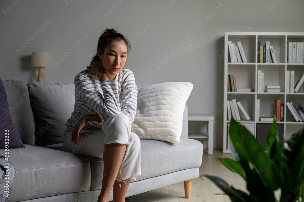 Young Asian woman sit on couch at home feeling sad tired and worried suffering depression in mental health. Female suffer from mental health problems.