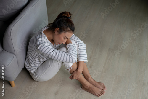 Lonely Asian woman in distress, worried, confused, sitting on floor at home. Female suffer from mental health problems.