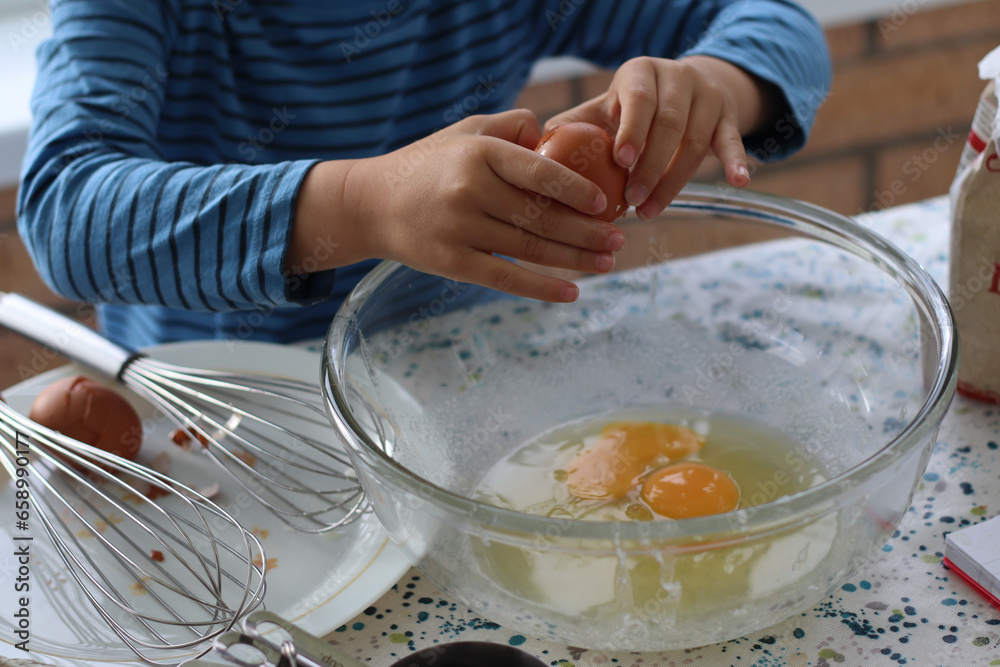Child broke fresh egg. Child hand cracking egg for cooking, baking cake, waffles at home in the kitchen. Fresh free range eggs in a glass bowl. Close up photo family lifestyle. Child broke fresh egg. Child hand cracking egg for cooking, baking cake, waffles at home in the kitchen. Fresh free range eggs in a glass bowl. Close up photo family lifestyle.