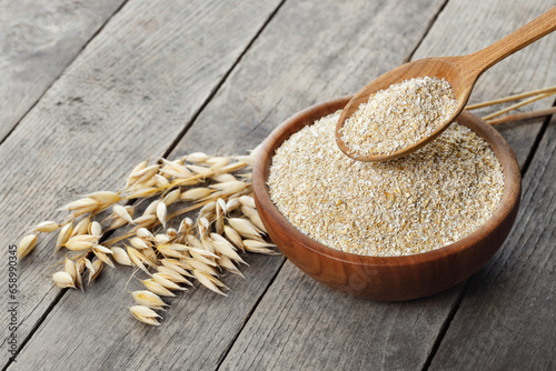 oat bran in bowl and in spoon with dry ears near on table