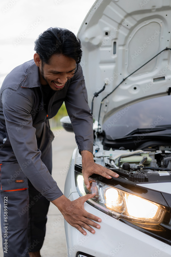 Auto mechanic inspects car by inspecting and writing checklist on clipboard. Mechanic checks car parts stock on laptop computer with car broken down on the side of the road Auto mechanic inspects car by inspecting and writing checklist on clipboard. Mechanic checks car parts stock on laptop computer with car broken down on the side of the road