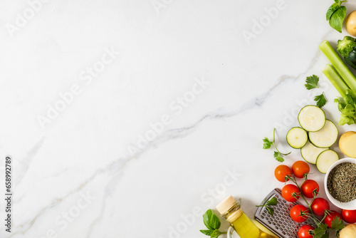 Top view healthy food cooking ingredients background with fresh vegetables, herbs, spices and olive oil on marble table with copy space