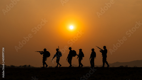 silhouette group of special forces sodiers walking and holding gun over the sunset and colorful orange sky background,