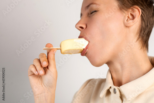 A woman in her middle years enjoys ice cream against a pristine white background, relishing the frozen delight with each delightful lick