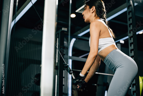 Woman holding onto the bar of a weight machine, using her arm strength to pull down and workout her muscles. fitness center health workout concept