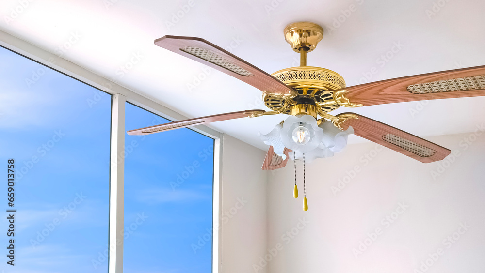 Vintage ceiling fan with electric lamps hanging on ceiling inside of white room