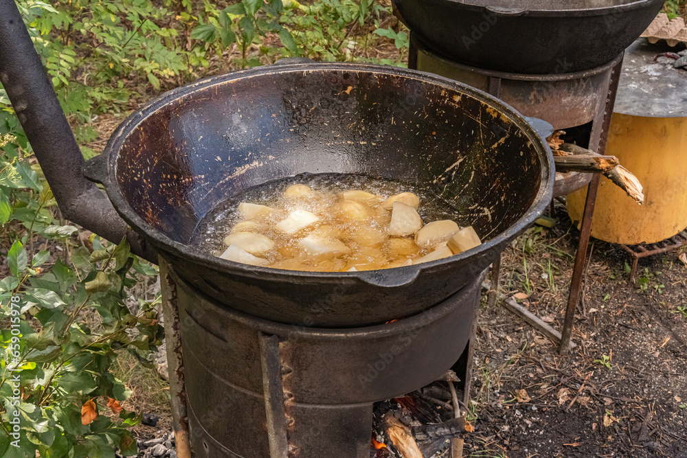 Coarsely chopped potatoes are fried in boiling oil in a cast-iron cauldron on a wood-burning stove. Street food Coarsely chopped potatoes are fried in boiling oil in a cast-iron cauldron on a wood-burning stove. Street food