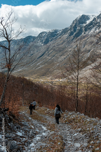 Group of friends hiking during fun travel in the mountains of Valbona Valley National Park, Albania full of snow, brown and orange leaves, during fall