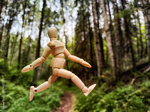 Wooden toy mannequin in the forest among grass and trees in summer, autumn, spring. The concept of outdoor recreation and hiking. Healthy lifestyle. Earth Day. Save planet concept. Partial focus, blur