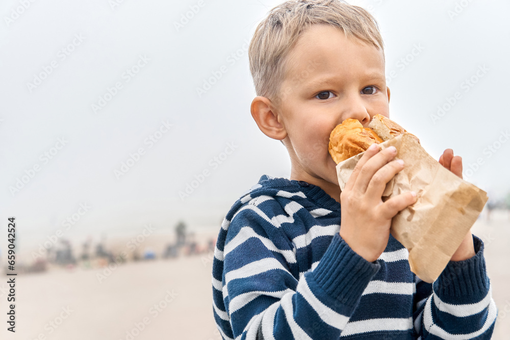 Hungry little boy with hood eats sandwich on misty day. Cute child bites snack resting in foggy highland. Kid has dinner outdoors Hungry little boy with hood eats sandwich on misty day. Cute child bites snack resting in foggy highland. Kid has dinner outdoors