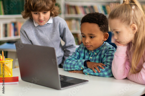Three diverse kids exploring on laptop in classroom