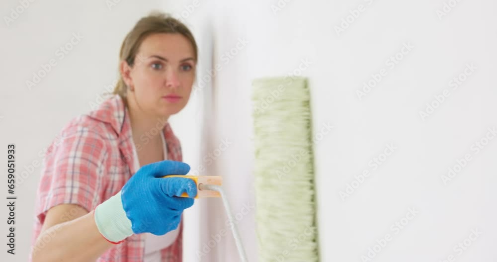 A woman makes repairs in the room. A girl paints a wall with a roller in white A woman makes repairs in the room. A girl paints a wall with a roller in white