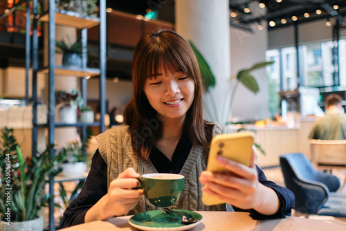 Young Asian woman looking at cell phone while having a coffee
