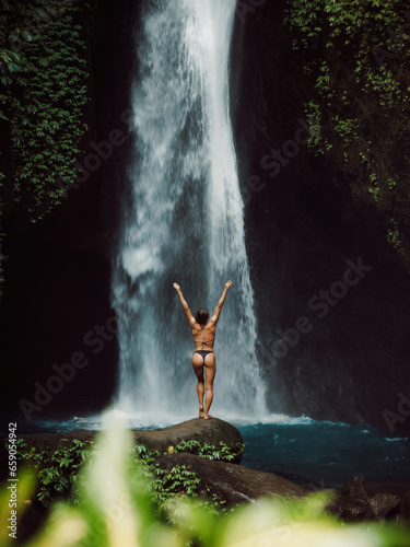 Waterfall and happy woman in bikini. Traveler girl posing on waterfall