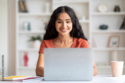 Positive young hindu lady freelancer working on laptop from home