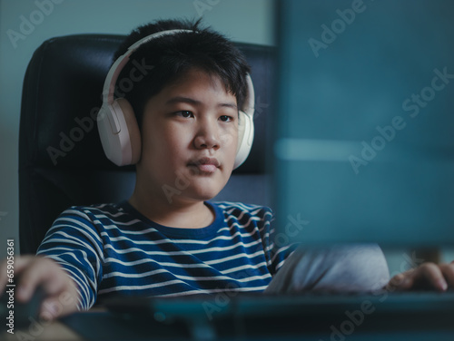 Lifestyle Asian little boys smile use desktop PCs computer to play professional video games with headphones in the house, Chat with friends, and Entertainment