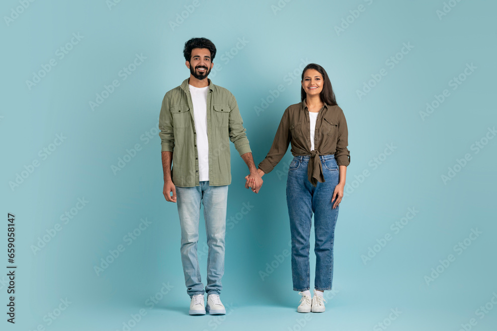Beautiful young indian couple posing on blue, holding hands