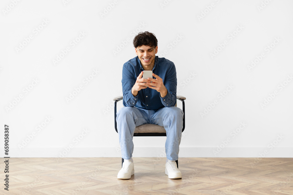 Middle eastern young man texting on smartphone over white wall