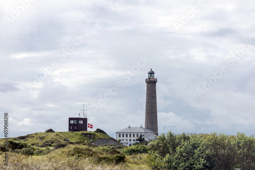 Natural landscape with lighthouse. Sand dunes covered with bushes and grass.