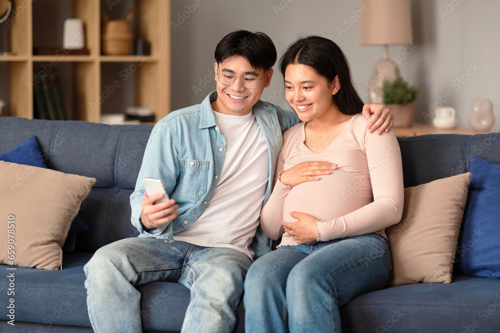 Happy Asian Man And Pregnant Woman Using Smartphone At Home Happy Asian Man And Pregnant Woman Using Smartphone At Home