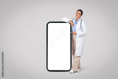 Latin woman doctor by huge cellphone with blank screen., mockup