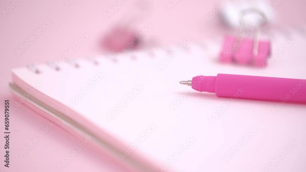 pink ballpoint pen and paper clips lying on a pink notepad with a blank page. closeup rotation. concept of stationery and school supplies. back to school. selective focus. pink ballpoint pen and paper clips lying on a pink notepad with a blank page. closeup rotation. concept of stationery and school supplies. back to school. selective focus.
