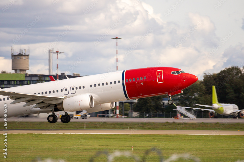 An aircraft with a red-colored bow takes off from the airfield runway An aircraft with a red-colored bow takes off from the airfield runway