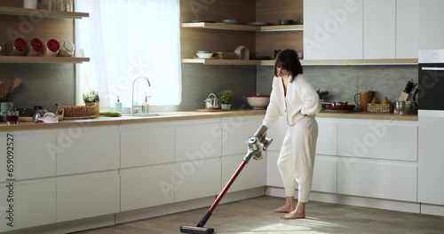 A displeased woman uses a vacuum cleaner in the kitchen. Her discontent is evident as she carries out the cleaning task, creating a less-than-pleasant atmosphere in the kitchen. photo