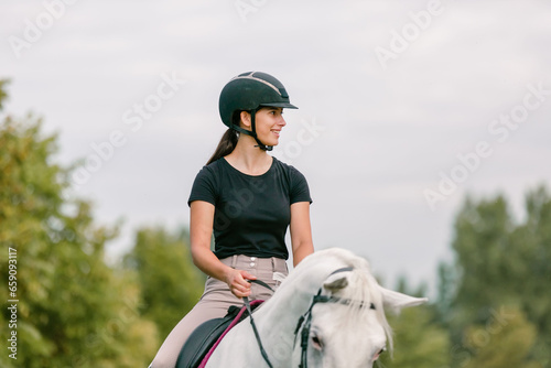 Pretty girl, a horseback rider riding beautiful snow white horse, walking along a path on a sunny summer day