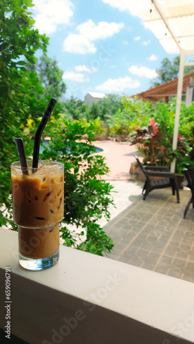 Vertical view of a glass of iced cappuccino perched on a veranda of a resort on a hot summer day