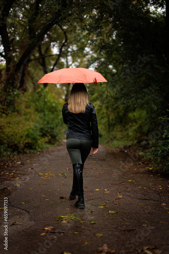 A girl walking in the park under an umbrella in the fall. A red umbrella in the fall